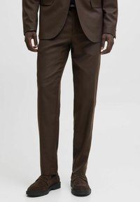 Pantaloni maro, croiți pe corp, dintr-un material neted, cu un croi drept și detalii minime, asortați cu pantofi slip-on din suede maro închis.