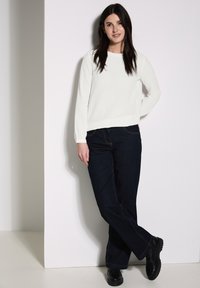 Witte geribbelde lange mouw top gecombineerd met donkerblauwe flare jeans en zwarte schoenen. De top heeft een ronde halslijn en een gestructureerde stof.