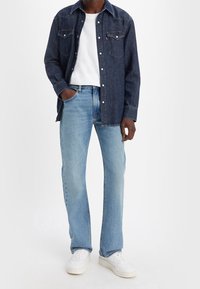 Camisa de botón de mezclilla oscura con bolsillos en el pecho, combinada con jeans rectos de mezclilla azul claro y zapatillas blancas. Diseño simple y casual.