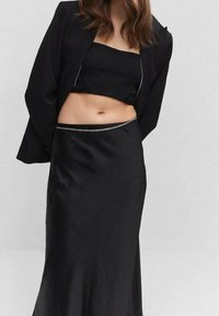 Schwarzes zweiteiliges Outfit mit einem Crop-Top und einem fließenden Rock, das an der Taille mit einer subtilen Kettenakzentuierung versehen ist und aus einem glatten, matten Stoff gefertigt ist.