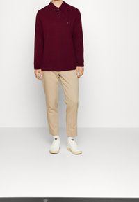 Bordeaux langærmet polo skjorte med knaplukning; parret med beige tapered bukser og hvide sneakers. Bomuldsstof, glat tekstur.