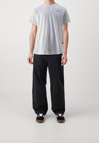 Světlé šedé bavlněné tričko s kulatým výstřihem, se zdobením v podobě malého červeného loga. Kombinováno s černými širokými kalhotami a černými teniskami s hnědými podrážkami.