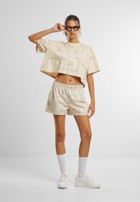 Beiger, verkürzter Oberteil und passende Shorts mit Blumenmuster, mit kurzen Ärmeln, lockerer Passform, kombiniert mit weißen Sneakers und Socken.