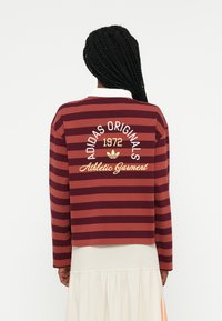 Bordo in burgundske črtaste dolge rokave polo majice z belim ovratnikom, ki vsebuje zlato vezenje "Adidas Originals 1972" in "Athletic Garment".
