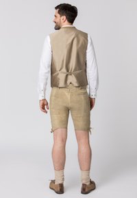Beige satijnen vest over een wit shirt, gecombineerd met beige leren shorts met strikjes aan de onderkant. Bruine veterschoenen en geribde sokken.