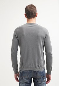 Szary sweter z dzianiny z długimi rękawami, okrągłym dekoltem, teksturowaną tkaniną i ściągaczami na rękawach, noszony na niebieskich dżinsach.