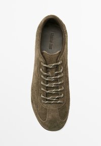 Olive green suede sneaker featuring round laces, a textured upper, and a reinforced toe. Subtle branding embossed on the insole.