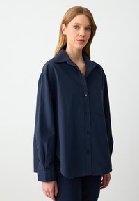 Navy blue button-up shirt in lightweight cotton, featuring a chest pocket, long sleeves, and a classic collar with a relaxed fit.
