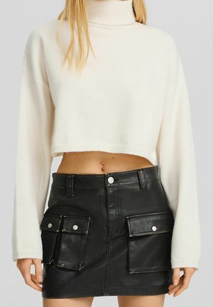 Cropped white turtleneck sweater with long sleeves, paired with a black leather mini skirt featuring two front pockets and silver hardware.