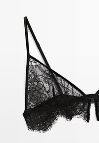 Black lace bralette featuring floral patterns, adjustable straps, and a hook-and-eye closure. The bottom edge has a fringed detail.