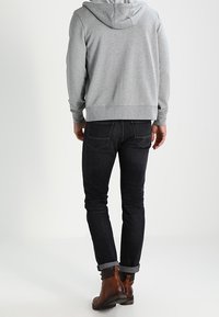 Grau Hoodie mit lockerer Passform, schwarze Jeans und braune Lederstiefel. Die Jeans haben einen Slim-Fit-Schnitt und hochgekrempelte Säume, die einen lässigen Stil zur Geltung bringen.