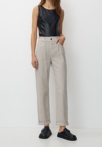 Haut sans manches noir en simili cuir, associé à un pantalon taille haute gris clair. Le pantalon dispose de poches avant et de revers. Sabots noirs avec des clous.