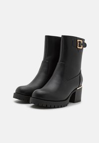Bottes noires en cuir à la cheville avec une surface texturée, dotées d'un détail de boucle sur le côté et d'un talon épais et rainuré pour plus de stabilité.