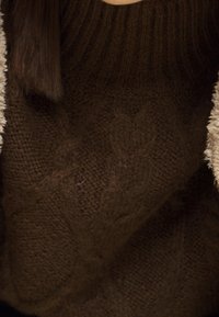 Brązowy sweter z dzianiny z fakturowanym wzorem w warkocze i szerokim ściągaczem na dekolcie. Miękka tkanina o grubym, przytulnym wyglądzie.