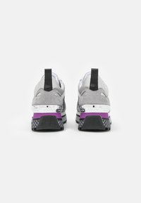 Sneaker grigie e bianche con una tomaia testurizzata, accenti neri e suola viola. Presentano un passante e un marchio sulla parte posteriore.