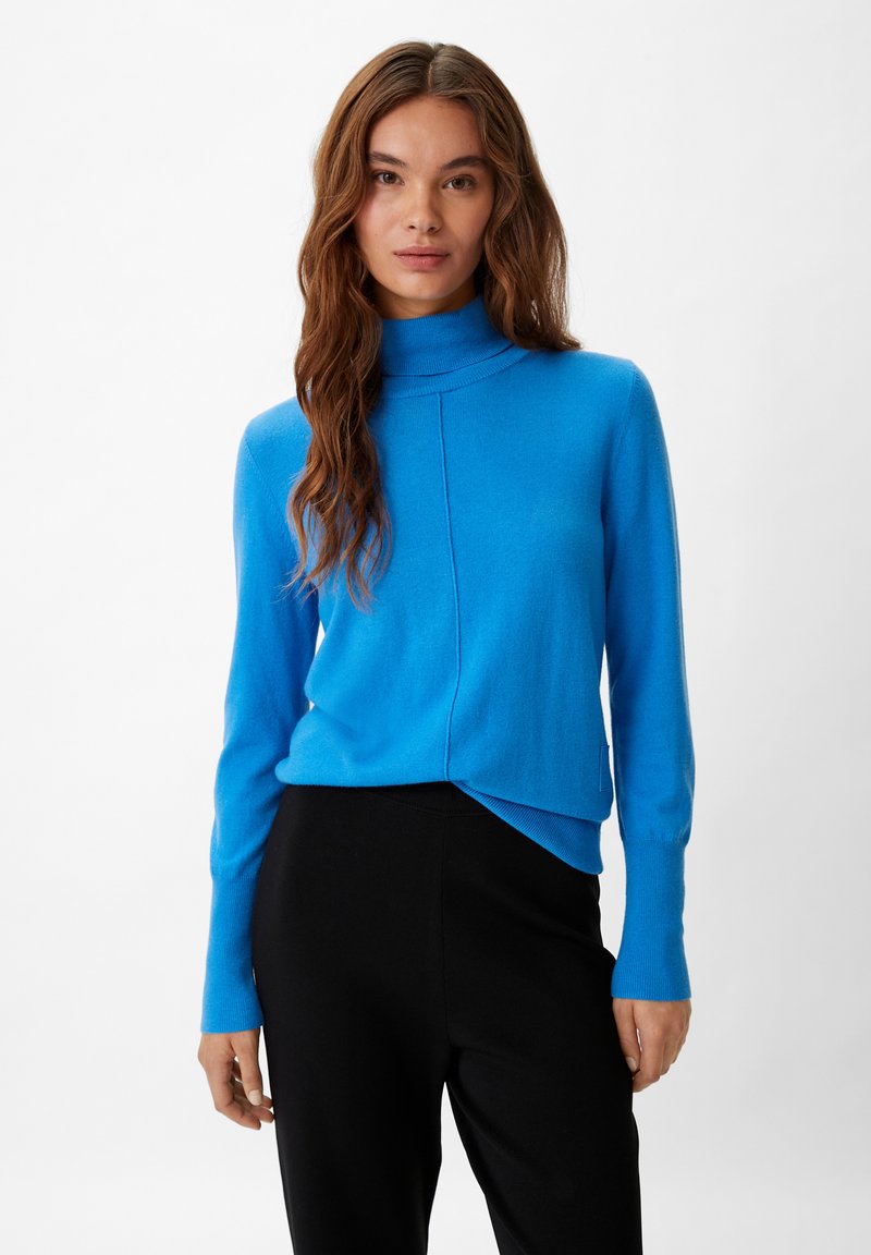 Blaues Rollkragensweatshirt aus weichem Material mit taillierter Passform, langen Ärmeln und asymmetrischem Saum, kombiniert mit schwarzen Hosen.
