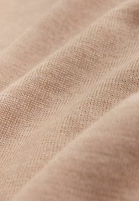 Hellbeiges, strukturiertes Gewebe mit diagonalen Falten, das ein weiches Webmuster und einen leichten Glanz aufweist. Das Material wirkt glatt und leicht.