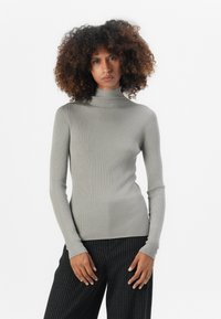 Ribbete turtleneck-genser i lys grå, med lange ermer og en tettsittende silhuett. Kombinert med svarte stripete bukser.