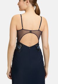 Granatowa sukienka wieczorowa z przezroczystym tyłem i ozdobnymi detalami po bokach, z cienkimi regulowanymi ramiączkami i dopasowanym fasonem.