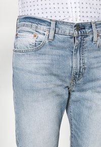 Ljusblå denimjeans med en klassisk femficksdesign. Har en knappstängning och subtila blekningar med en slät textur.