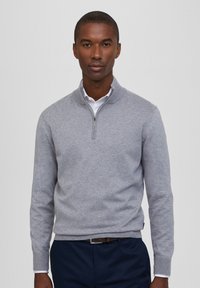 Hellgrauer Pullover mit hohem Kragen, ausgestattet mit einem halben Reißverschluss an der Vorderseite, gerippten Bündchen und Saum; glatte Textur und figurbetonter Schnitt.