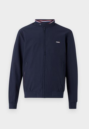 Tumed sinine kerge lukuga jakk kõrge kraega, elastsete mansettidega, kaks küljetaskut ja kontrastsete punaste ja siniste triibuga aktsendid.