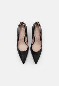 Talons hauts en cuir noir avec un bout pointu, texture lisse et doublure intérieure crème ; présente un branding minimal sur la semelle intérieure.