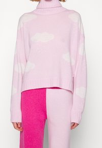 Heller rosa Pullover mit weißen Wolkenmustern, mit hohem Kragen, gerippten Bündchen und lässigem Schnitt. Kombiniert mit pinken und hellrosa Hosen.