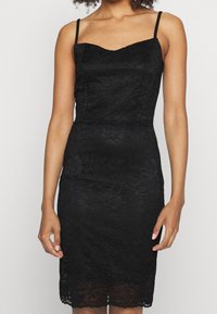 Svart spetsklänning med figursydd överdel, tunna axelband och vågig fåll. Har ett blommigt spetshmönster och en subtil lyster.