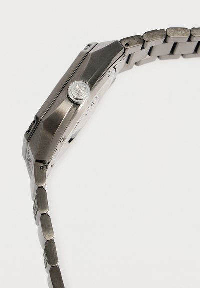 Vue latérale d'une montre-bracelet en acier inoxydable avec un bracelet à maillons et une couronne détaillée gravée d'un emblème de lion.