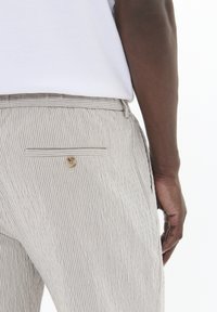 Pantalones de rayas beige hechos de tejido ligero, con un bolsillo trasero con cierre de botón y una superficie texturizada.