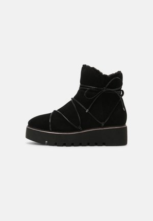 Botte de cheville en suède noir avec une finition texturée, dotée d'une semelle plateforme épaisse et de détails de lacets croisés sur le dessus.