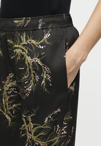Κοντινό πλάνο χεριού σε τσέπη μαύρου παντελονιού με ελαστική μέση με πράσινο και ροζ βοτανικό μοτίβο.