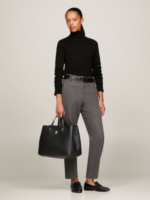 Svart polotröja, grå skräddarsydda byxor, svart läderhandväska med texturerad yta och silvriga detaljer, svarta loafers.