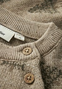 Beżowy sweter dziany z ribbanym kołnierzem, drewnianymi guzikami i subtelnym wzorem z ciemnozielonymi akcentami. Widoczna metka pielęgnacyjna.