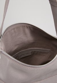 Šedá látková kabelka se zipovým uzávěrem, s hladkým vnějším povrchem a podšívkou uvnitř. Viditelná logo visačka uvnitř.