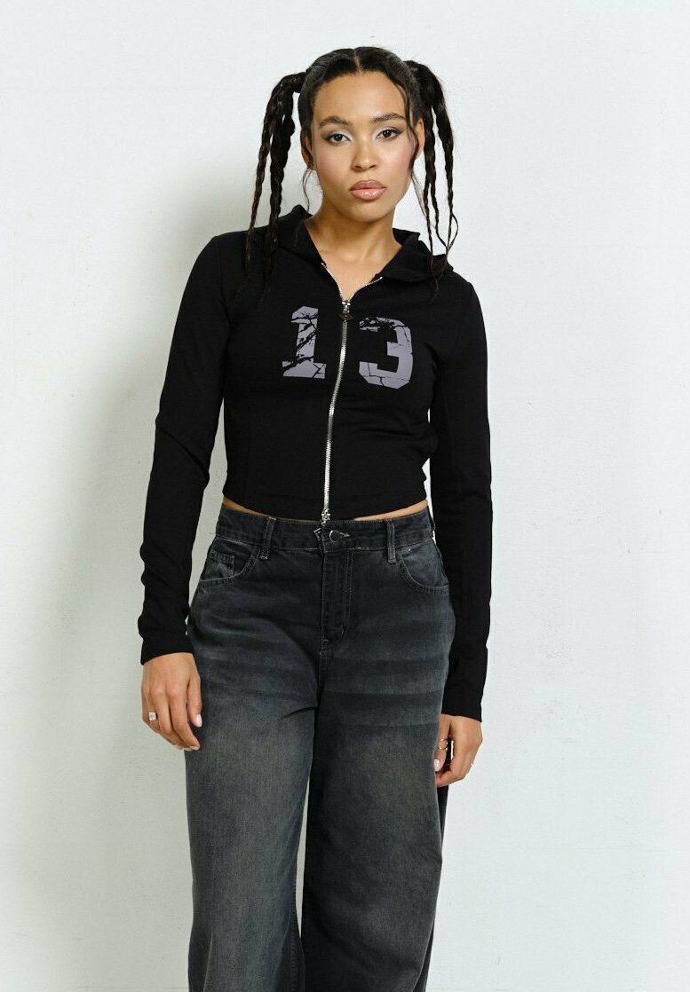 Czarna, krótka bluza z zamkiem błyskawicznym z grafika w kolorze szarym zniszczonym "13", zestawiona z wysokim stanem ciemnoszarymi spodniami typu wide-leg.