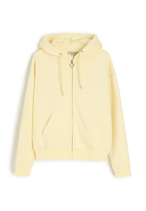 Jasnożółta bluza z kapturem na zamek błyskawiczny, z przednimi kieszeniami, kapturem ze sznurkiem i srebrnym suwakiem w kształcie pierścienia, pokazana na białym tle.