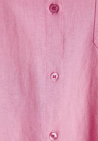 Svetlo roza lanena srajca z gladko teksturo, sprednjim zapenjanjem z ujemajočimi roza gumbi in podrobnostmi na žepu na prsih.