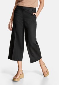 Svarta vida cropped-byxor med en slät yta, sidofickor och midjan är figurnära. Bärs med beigefärgade platåsandaler.