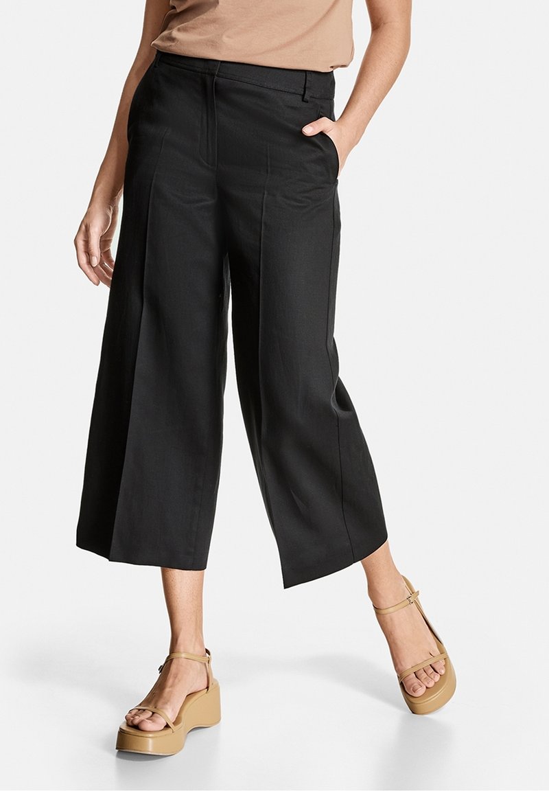 Svarta vida cropped-byxor med en slät yta, sidofickor och midjan är figurnära. Bärs med beigefärgade platåsandaler.