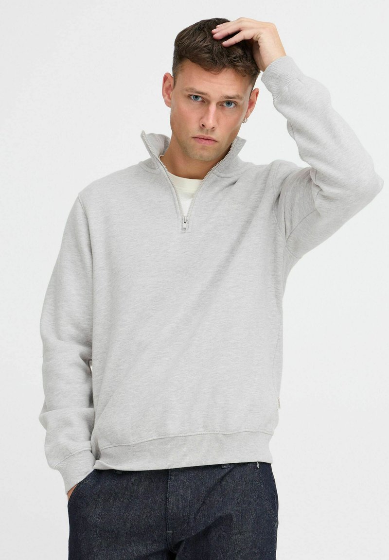 Lichtgrijze sweatshirt met een halve rits kraag, ribgebreide manchetten en een ribgebreide zoom. Het materiaal lijkt zacht en gemêleerd, geschik voor casual kleding.