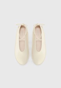 Ballerines couleur crème en cuir lisse, avec un bout arrondi et un délicat nœud à l'avant. Semelle plate.