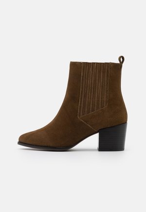 Bottine en daim marron avec talon bloc, panneau latéral élastique avec couture verticale et une languette à l'arrière.