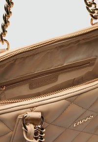 Borsa a tracolla beige trapuntata con hardware dorato. Caratterizzata da una catena, chiusura con zip e tasche interne. Etichettata con "LIU JO."