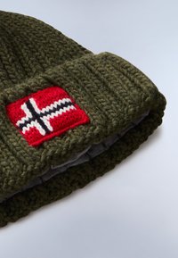 Gorro de punto verde con un prominente parche rojo que presenta un diseño de la bandera noruega en blanco y negro, texturizado y doblado en la base.