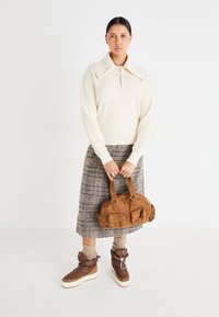 Suéter de punto crema con un gran cuello, falda acampanada a cuadros, bolso de corduroy marrón y botas aislantes marrones con suelas blancas.