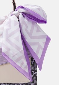 Lila kuviollinen silkkihuivi sidottuna käsilaukkuun, jossa on karheaa käärmeennahkakuosi ja sileät beige-korostukset.