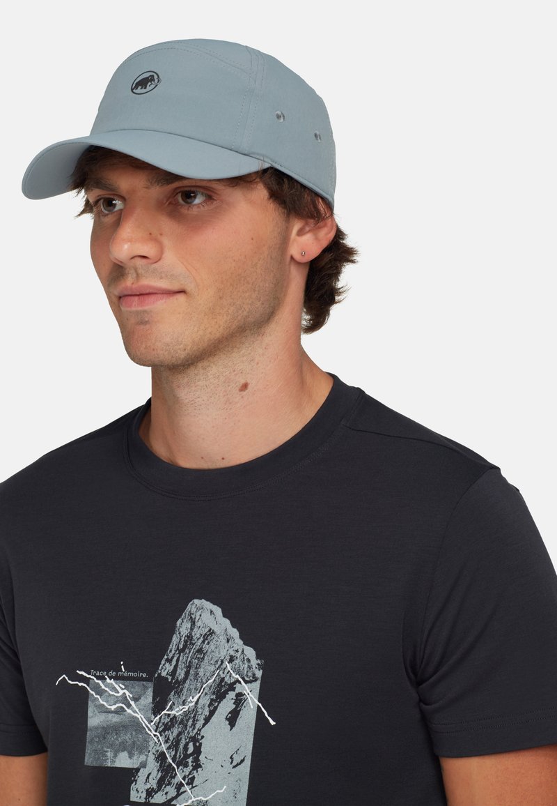 Lyseblå baseballcap med logo foran, med en buet skygge og syet detaljer, båret med en mørk t-shirt med grafik.