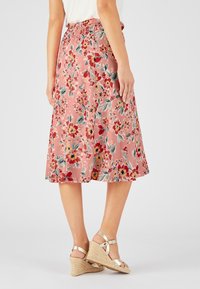 Falda midi floral en rosa, con una cinturilla elástica, patrones de flores coloridos y un diseño acampanado. Llevada con sandalias de cuña.